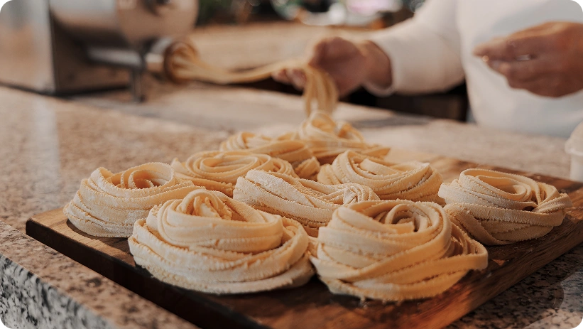 Nidi di pasta fresca fatta a mano disposti su un tagliere di legno mentre vengono preparati in una cucina italiana tradizionale.