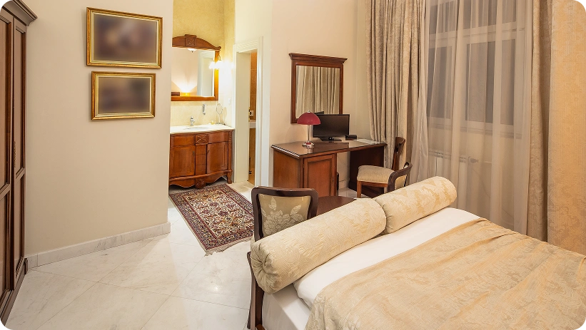Elegante camera d'hotel con letto matrimoniale, scrivania in legno, pavimento in marmo e un'area vanità aperta, progettata per un soggiorno confortevole.
