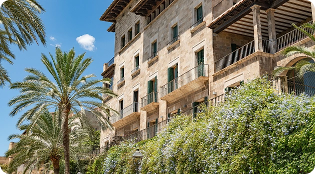 Elegante hotel in stile mediterraneo circondato da giardini lussureggianti, palme e piante fiorite.