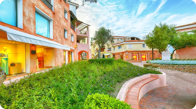 Affascinante cortile di un resort mediterraneo con negozi boutique, giardini paesaggistici e architettura tradizionale dai colori pastello.