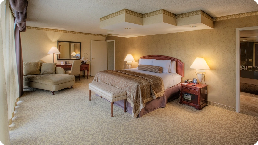 Ampia suite d'hotel con letto king-size, accogliente area salotto, scrivania e illuminazione ambientale calda.