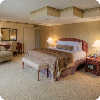 Ampia suite d'hotel con letto king-size, accogliente area salotto, scrivania e illuminazione ambientale calda.